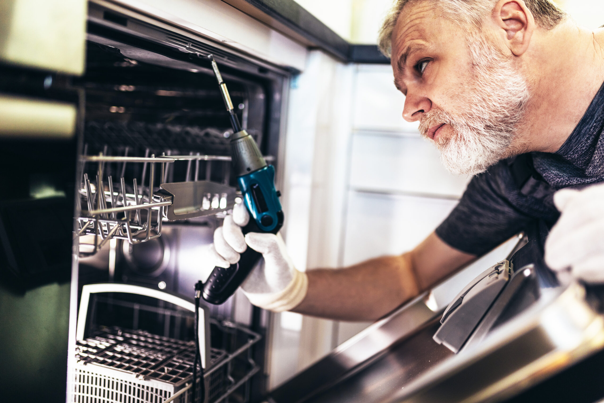 Man with toolbox repairing dishwasher in a household.