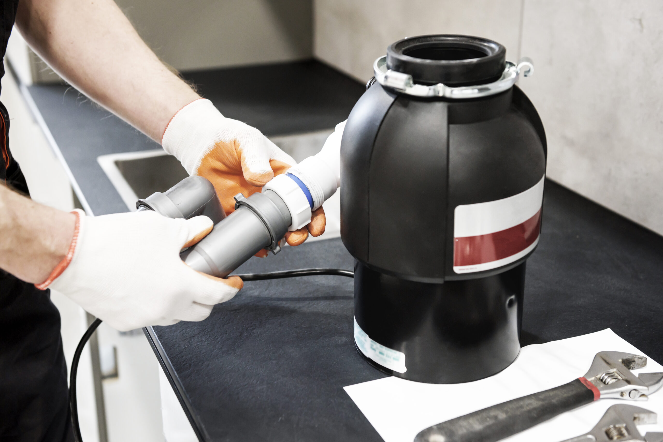 A worker is installing a household waste shredder for the kitchen sink.